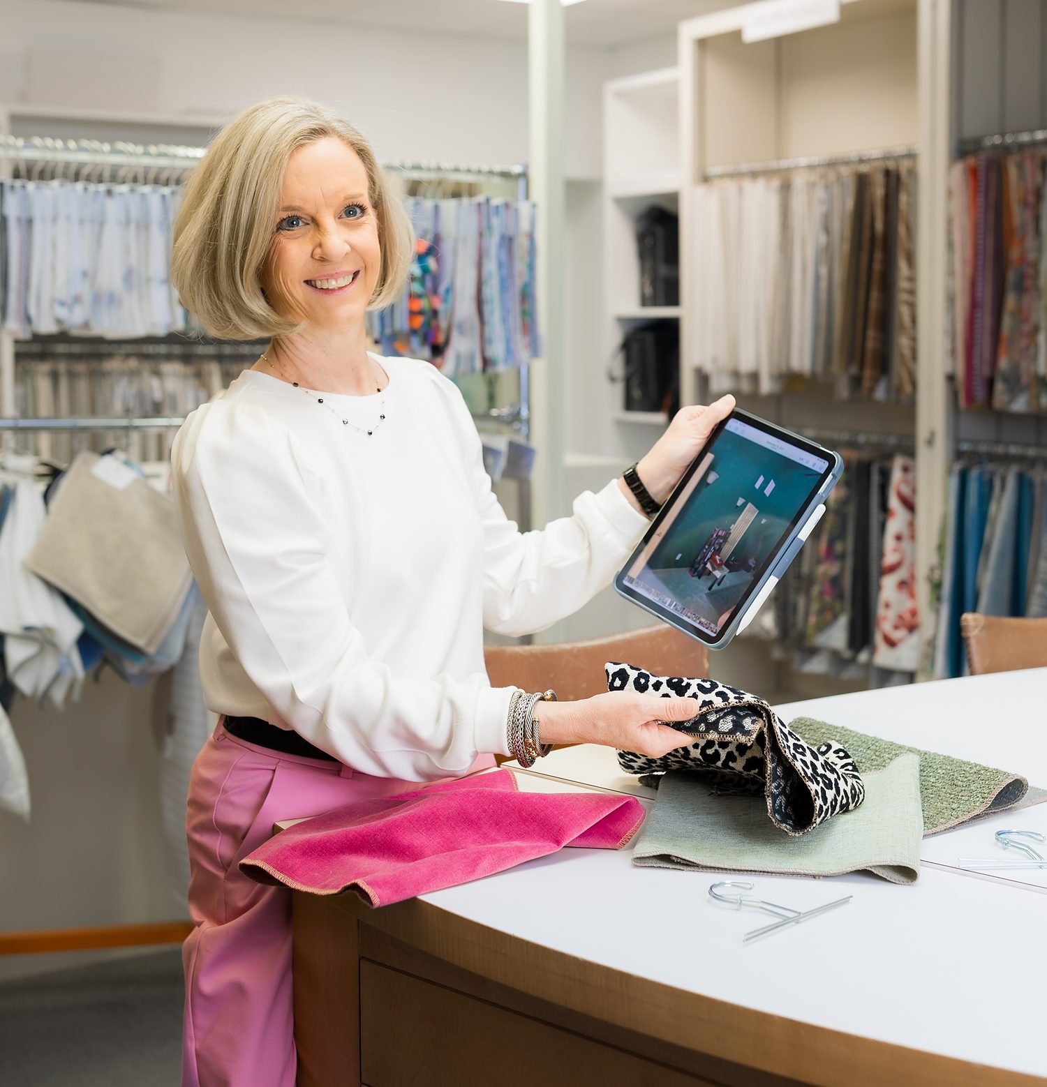 Kathy Adams designer presenting a room design on a tablet with fabric samples in the studio
