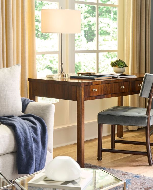 Walnut writing desk with a nickel lamp beside a linen sofa