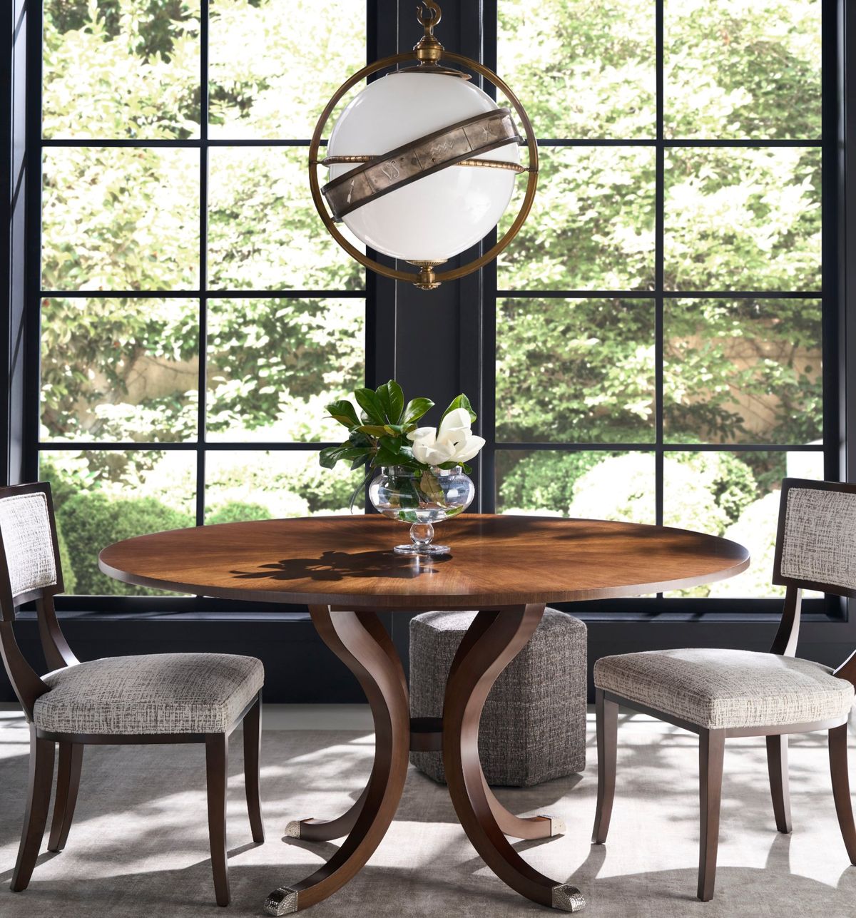 Round walnut pedestal dining table under a brass and glass globe pendant